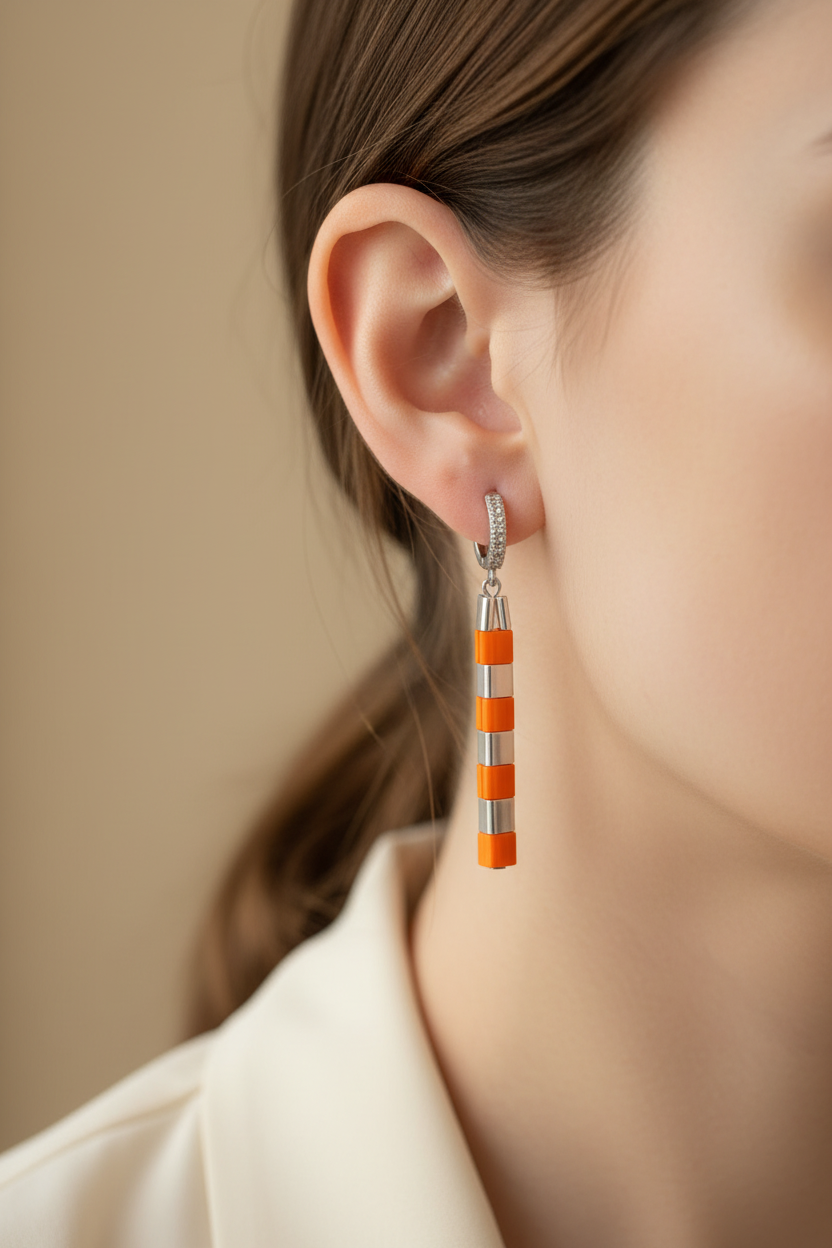 Woman wearing a geometric orange and silver Miyuki Tila drop earring.