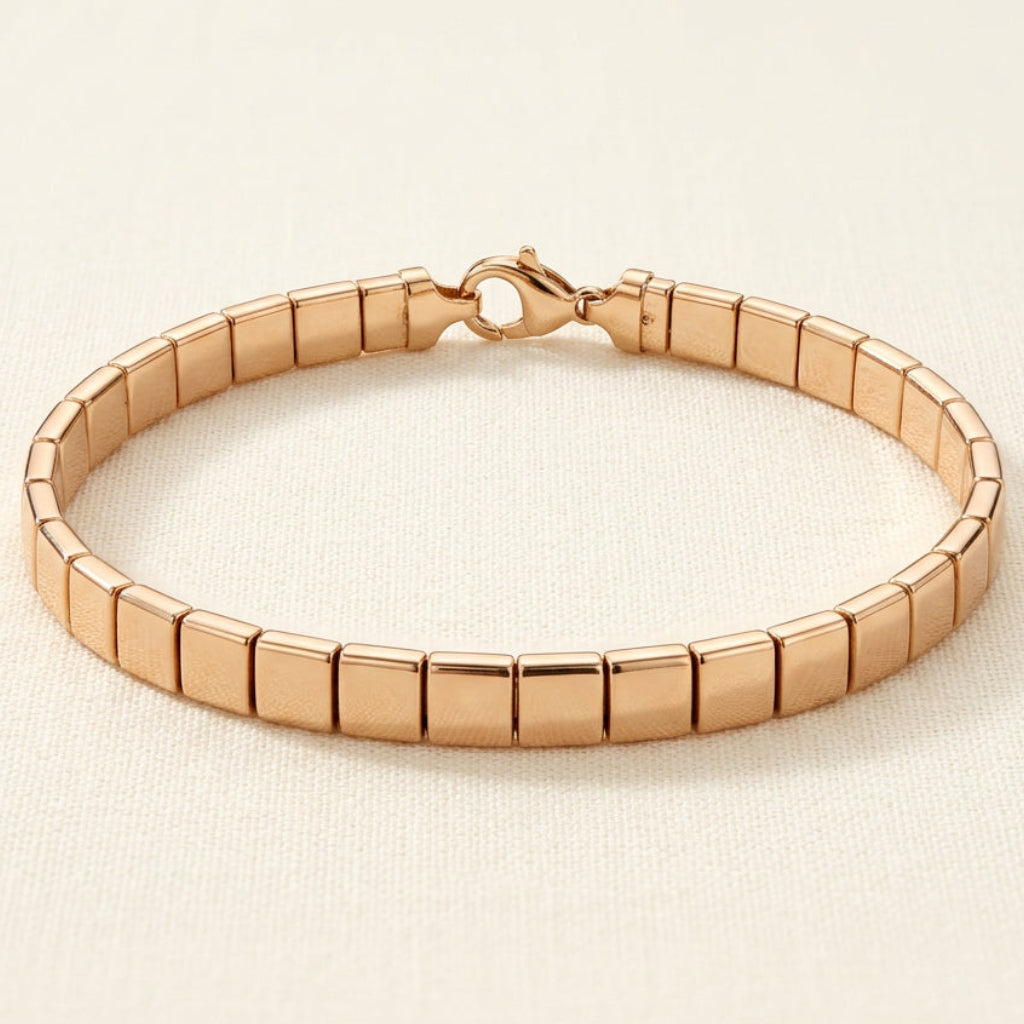 Aurum Line Slim bracelet with polished champagne gold-tone rectangular beads and a lobster clasp on cream fabric.

