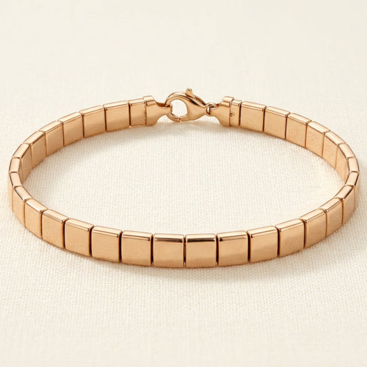 Aurum Line Slim bracelet with polished champagne gold-tone rectangular beads and a lobster clasp on cream fabric.

