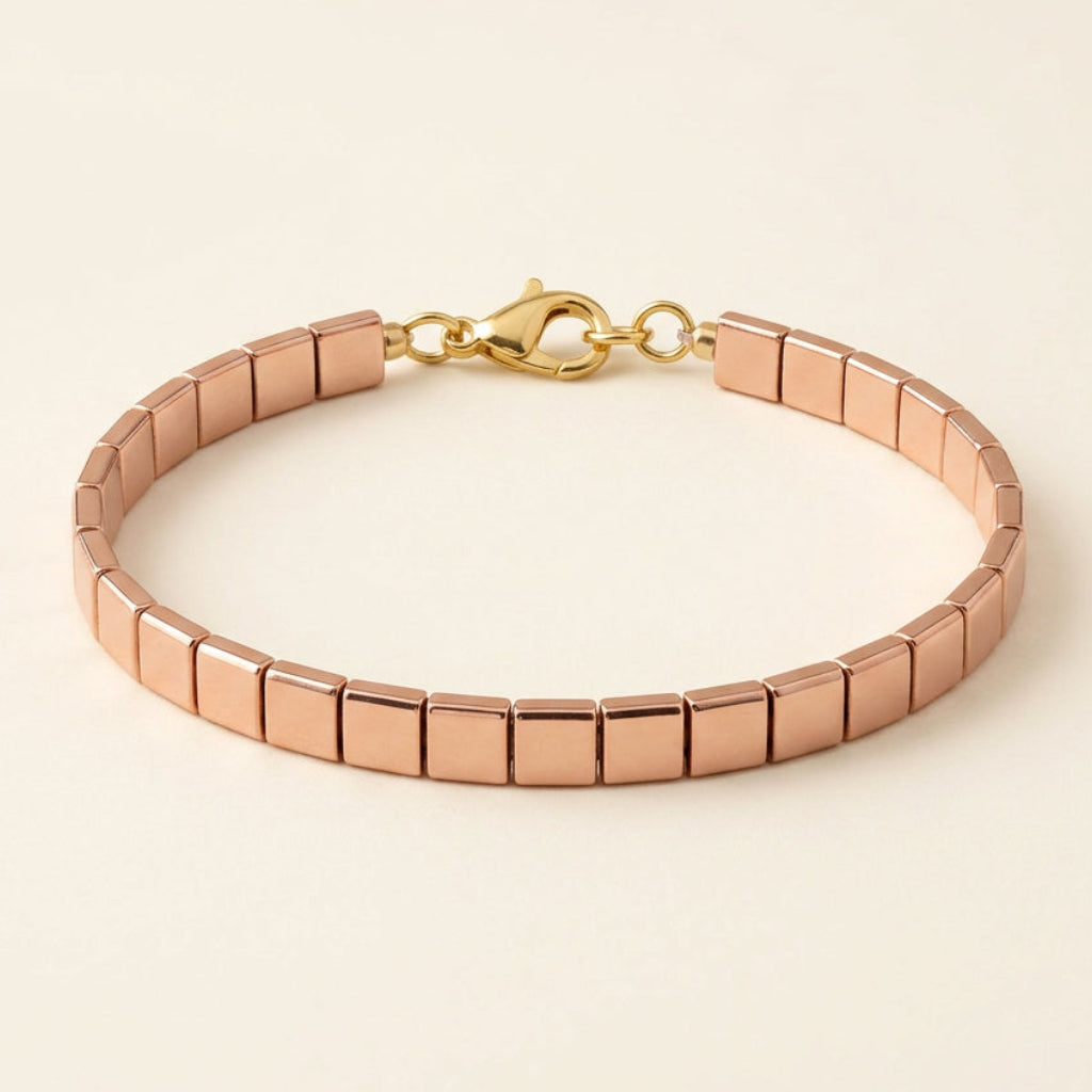 Aurum Line Slim bracelet with polished rose gold-tone rectangular beads and a lobster clasp on cream fabric.

