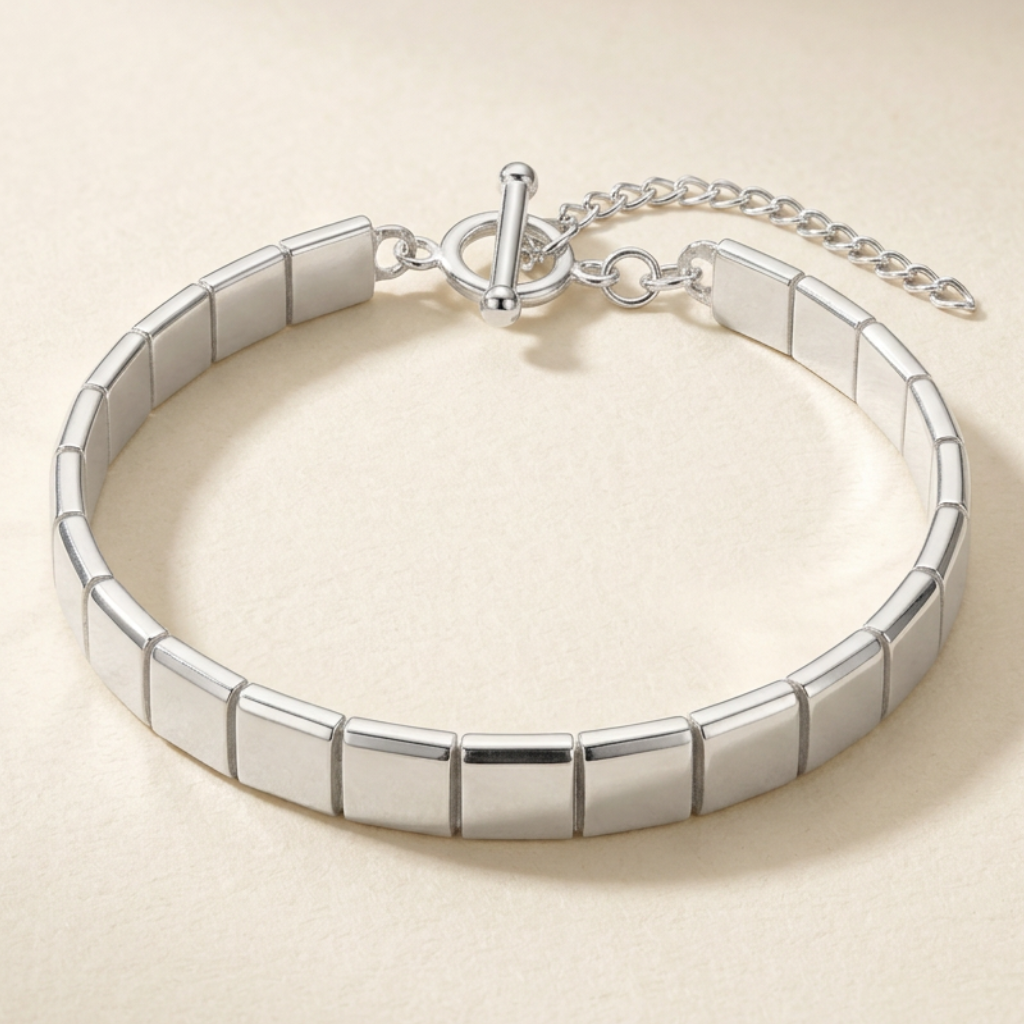 Aurum Line Slim bracelet with polished silver-tone rectangular beads and a lobster clasp on cream fabric.

