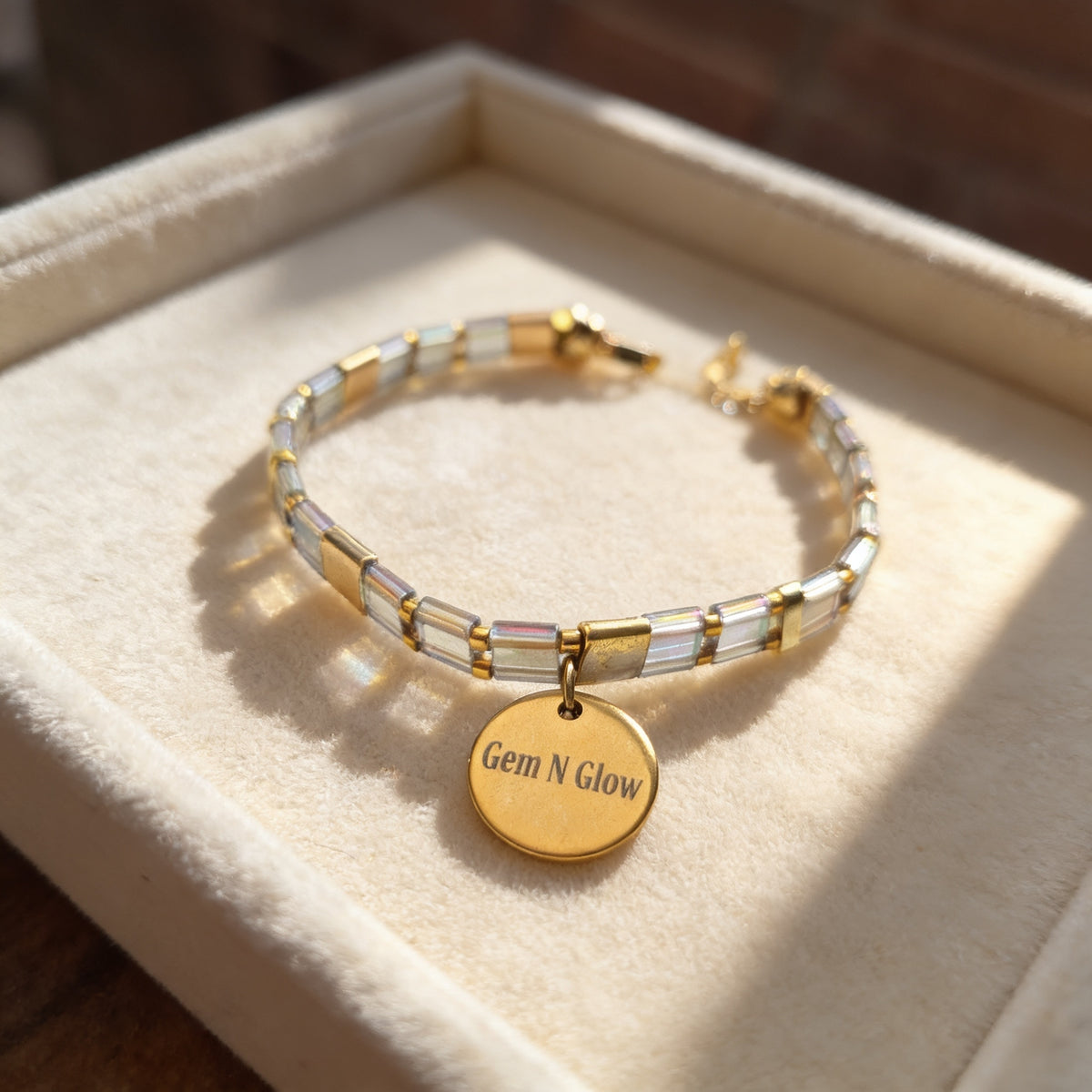Clear iridescent and gold-tone Miyuki Tila bracelet with a round Gem N Glow charm