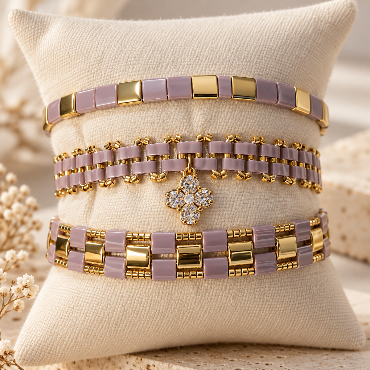 Three handmade lilac and gold Miyuki bracelets displayed together on an ivory cushion