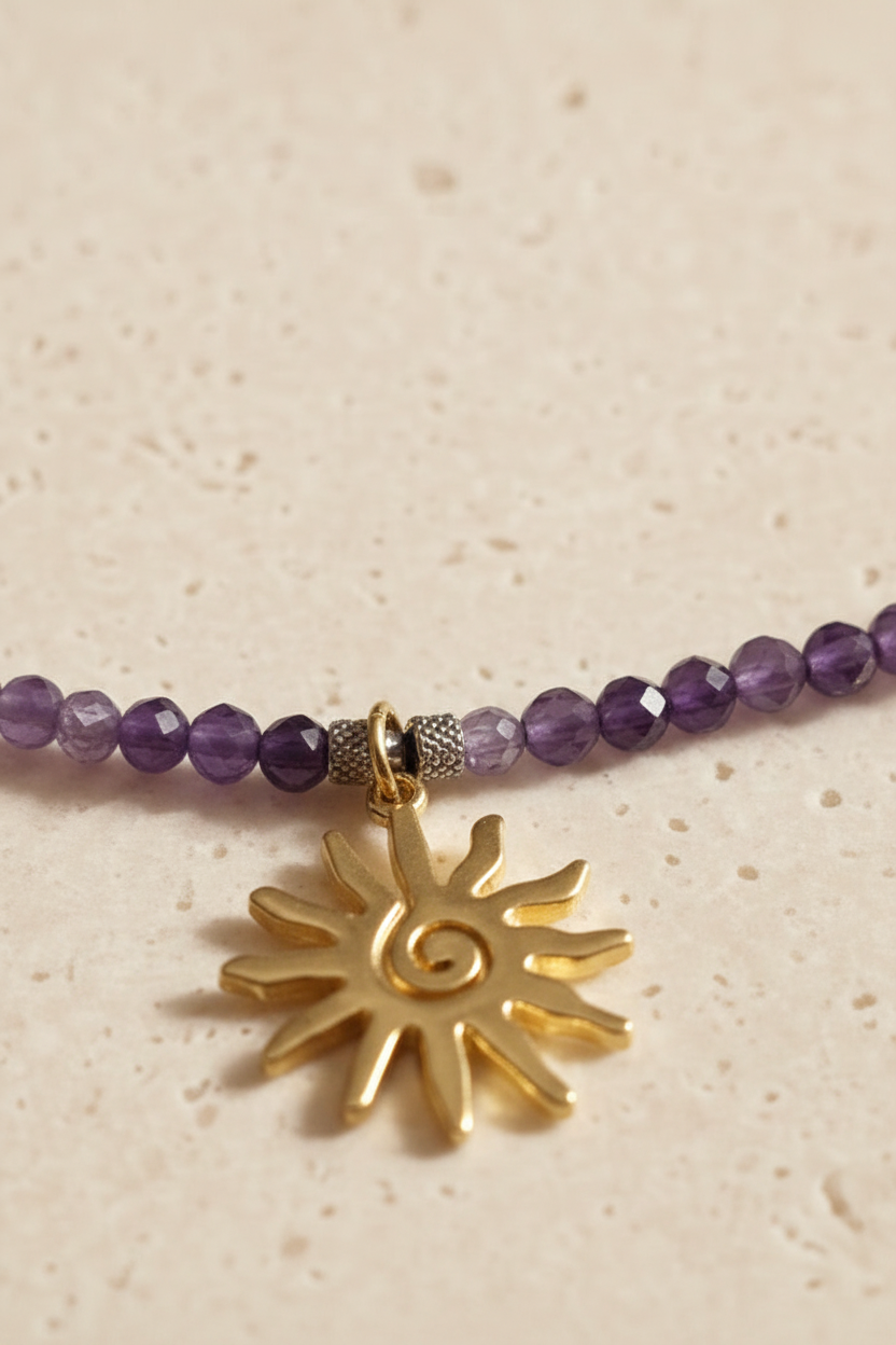 Close-up of faceted natural amethyst beads and gold sun pendant