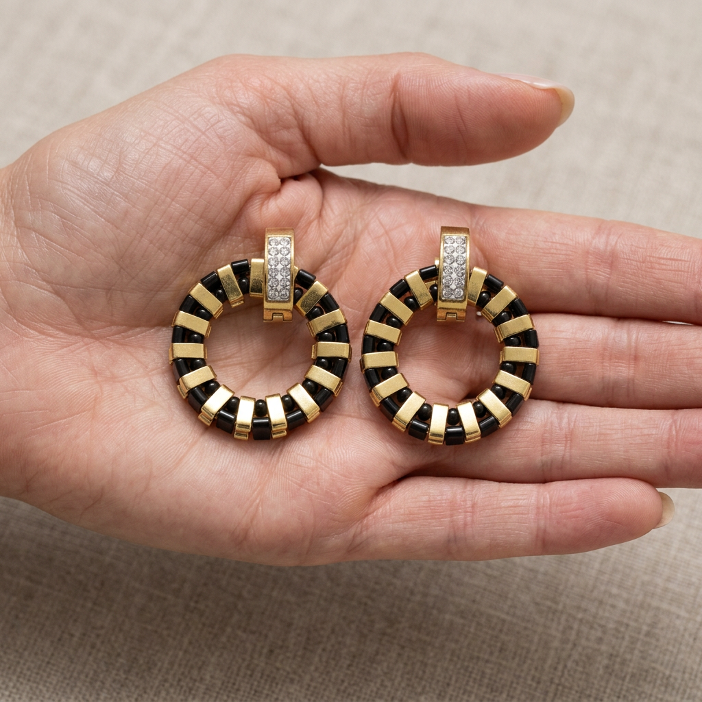 A pair of Noir Grid black and gold Miyuki Tila earrings resting in an open palm to show their scale.