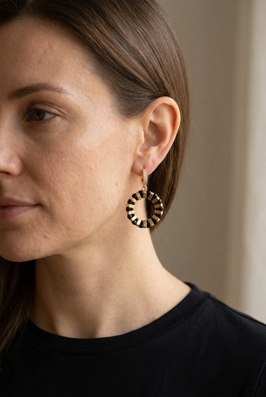 Noir Grid black and gold circular earring worn on an ear, showing the drop and cubic zirconia hoop