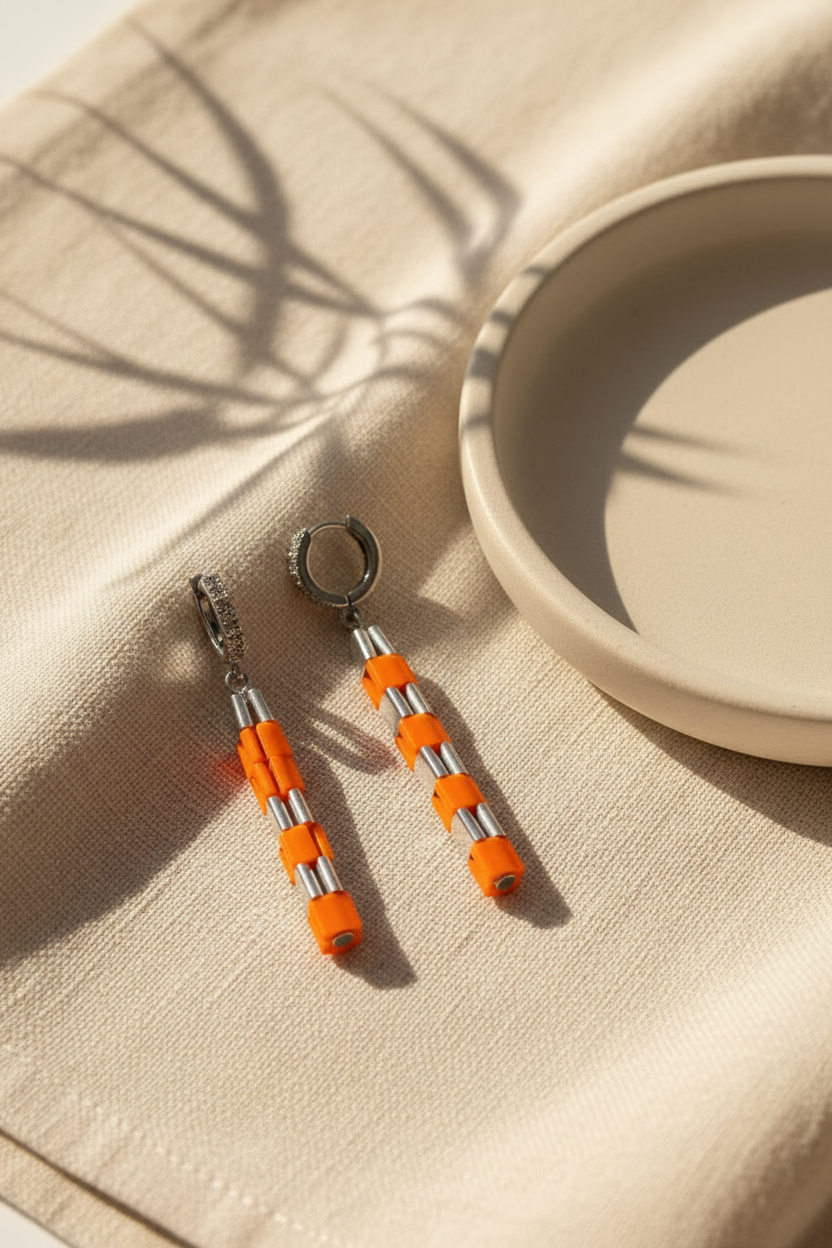 Orange and silver geometric beaded earrings styled on neutral ivory linen.