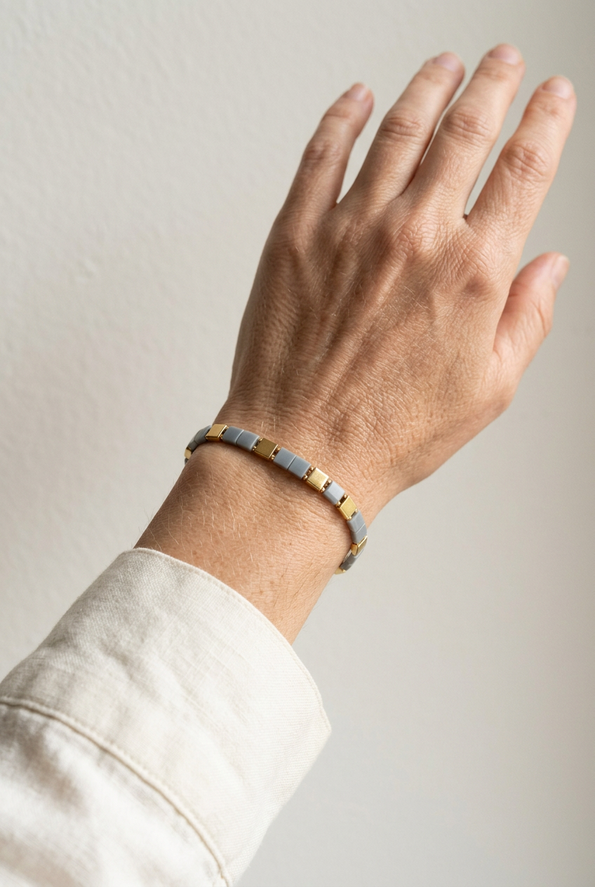 Vertex Slim grey and gold Miyuki bracelet worn alone on a wrist with an ivory sleeve.